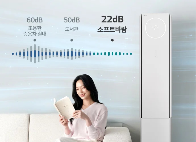 "해당 이미지는 에어컨의 소프트바람 기능에 대해 설명하는 이미지로 저소음 냉방 기능과 사용 환경을 시각적으로 보여주고 있습니다. 우측에 스탠드 에어컨이 배치되어 있으며, 여성 모델이 베이지색 소파에 앉아 책을 읽고 있습니다. 에어컨 상단의 원형 디지털 디스플레이에는 온도 정보가 표시되어 있습니다. 이미지 상단에는 소음 비교를 나타내는 그래픽과 함께 60dB 조용한 승용차 실내, 50dB 도서관, 22dB 뷰I 에어컨 이라는 문구가 순서대로 배치되어 있습니다."